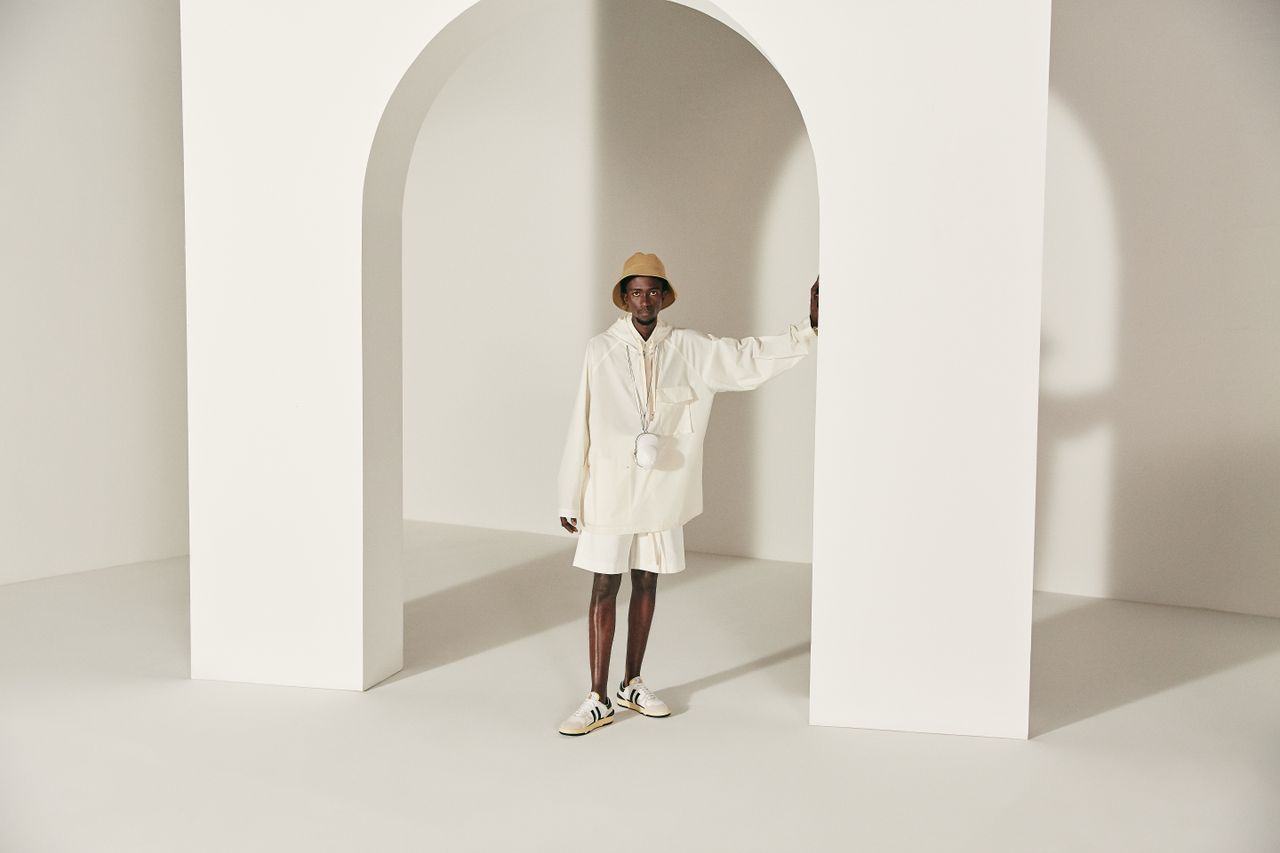 Stylish man in white attire posing by large arch in a modern studio.
